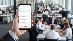 Smartphone zeigt die Markierungen einer Aufnahme, im Hintergrund eine Besprechung im Büro