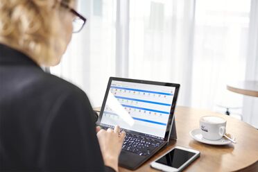 agorum Software 20 Jahre Jubiläum Ein Mitarbeiter von agorum Software GmbH arbeitet an einem Laptop im Café, während ein Cappuccino auf dem Tisch steht.