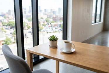 Heller Holzschreibtisch mit Kaffeetasse und kleiner Pflanze vor einem großen Fenster mit Stadtblick