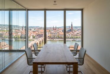 Heller Besprechungsraum mit Blick durch bodentiefe Fenster auf eine europäische Stadt mit Fluss und Brücke