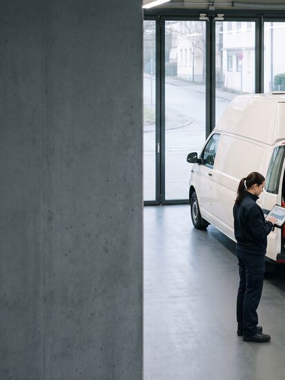 Drei Rettungskräfte mit Tablet vor einem Einsatzfahrzeug in der Fahrzeughalle