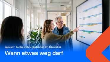 Zwei Personen stehen vor einem großen digitalen Kalender an der Wand, eine zeigt auf einen Termin