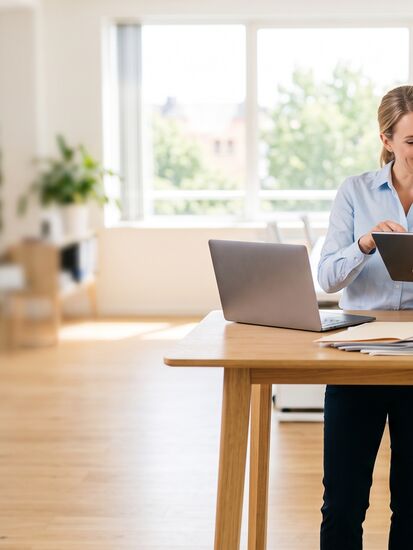 Zwei Sachbearbeiter stehen im Schadenbüro einer Versicherung an einem Stehtisch, sie hält ein Tablet, er blättert in einem Papierordner