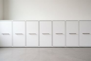 Reihe weißer Schrankfronten mit schlichten Edelstahlgriffen in einem hellen Raum