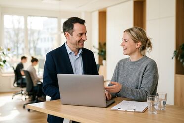 Berater und Interessentin stehen an einem Stehtisch und sprechen über ein aufgeklapptes Notebook
