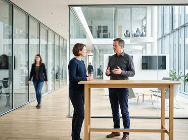 Zwei Personen im Gespräch an einem Stehtisch in einer offenen Bürozone