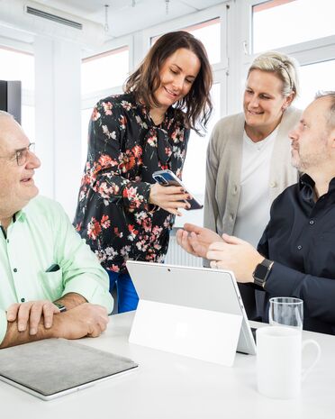 Vier Personen sitzen an einem Tisch und diskutieren über ein Dokumentenmanagement-System auf einem Tablet.