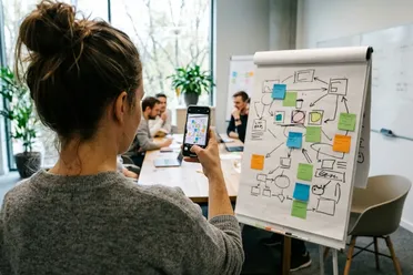 Frau fotografiert während einer Besprechung ein Flipchart mit dem Smartphone