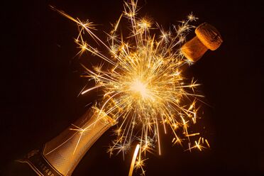 Eine Sektflasche mit herausspringendem Korken und Funkenflug, symbolisiert Neujahr und Feierlichkeiten.