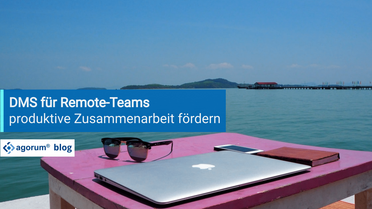 Ein Laptop, eine Sonnenbrille, ein Smartphone und ein Notizbuch liegen auf einem Tisch am Wasser, symbolisieren die Nutzung eines Dokumentenmanagementsystems für Remote-Teams.