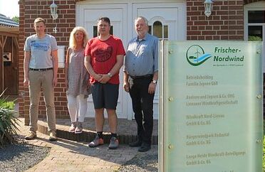 Team von Frischer Nordwind Das Team von Frischer Nordwind steht vor einem Gebäude, neben einem Schild mit Firmeninformationen.