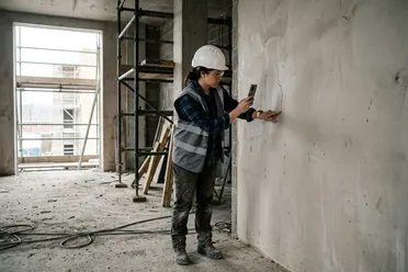 Bauleiterin fotografiert bei der Baustellenbegehung einen Riss in der Wand mit dem Smartphone