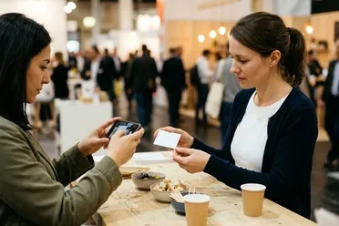 Ausstellerin fotografiert auf einer Messe die Visitenkarte einer Interessentin mit dem Smartphone
