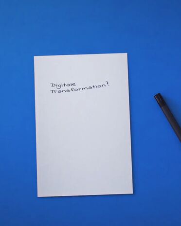 Ein Blatt Papier mit der Aufschrift 'Digitale Transformation?' liegt auf einem blauen Hintergrund neben einem Stift.