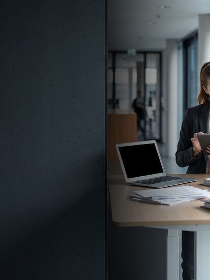 Zwei Sachbearbeiter stehen im Schadenbüro einer Versicherung an einem Stehtisch, sie hält ein Tablet, er blättert in einem Papierordner