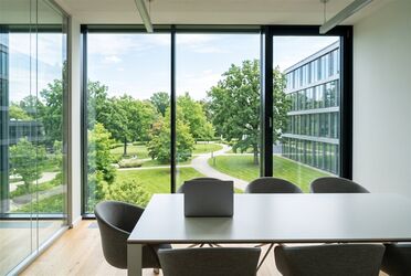 Heller Besprechungsraum mit Laptop auf dem Tisch und Blick auf einen grünen Firmencampus