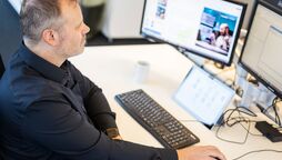 Support-Arbeitsplatz bei agorum core Ein Mitarbeiter arbeitet an einem Schreibtisch mit mehreren Monitoren, die das Dokumentenmanagement-System anzeigen.