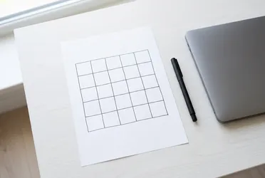 Weißes Blatt mit handgezeichnetem Raster aus fünf Spalten und fünf Zeilen auf einem hellen Schreibtisch als Datenlandkarte